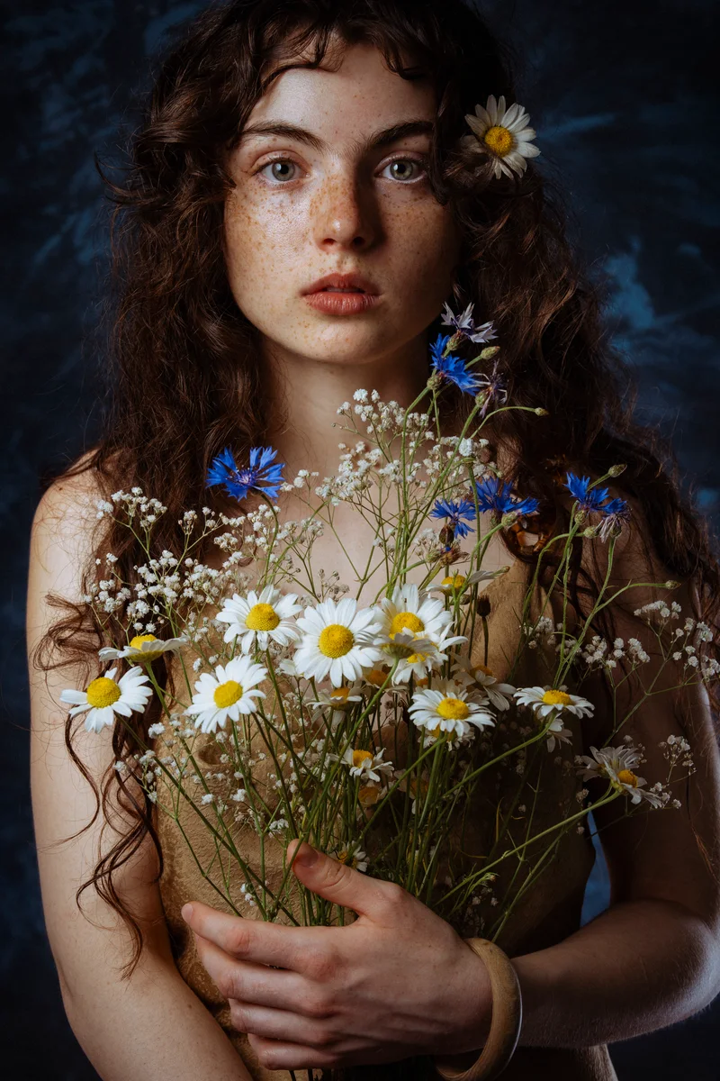 Curly-haired woman holding wildflowers and daisies against a dark backdrop