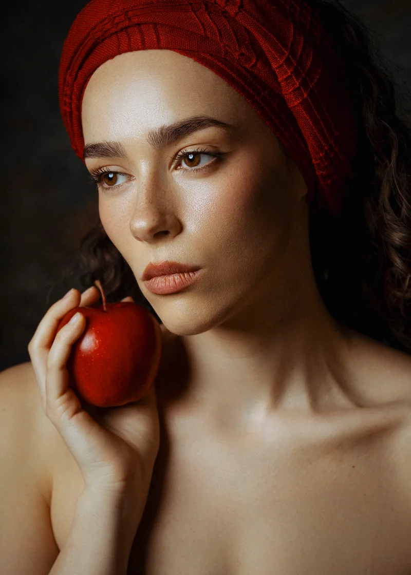 Woman with a red knitted headwrap holding a red apple to her cheek