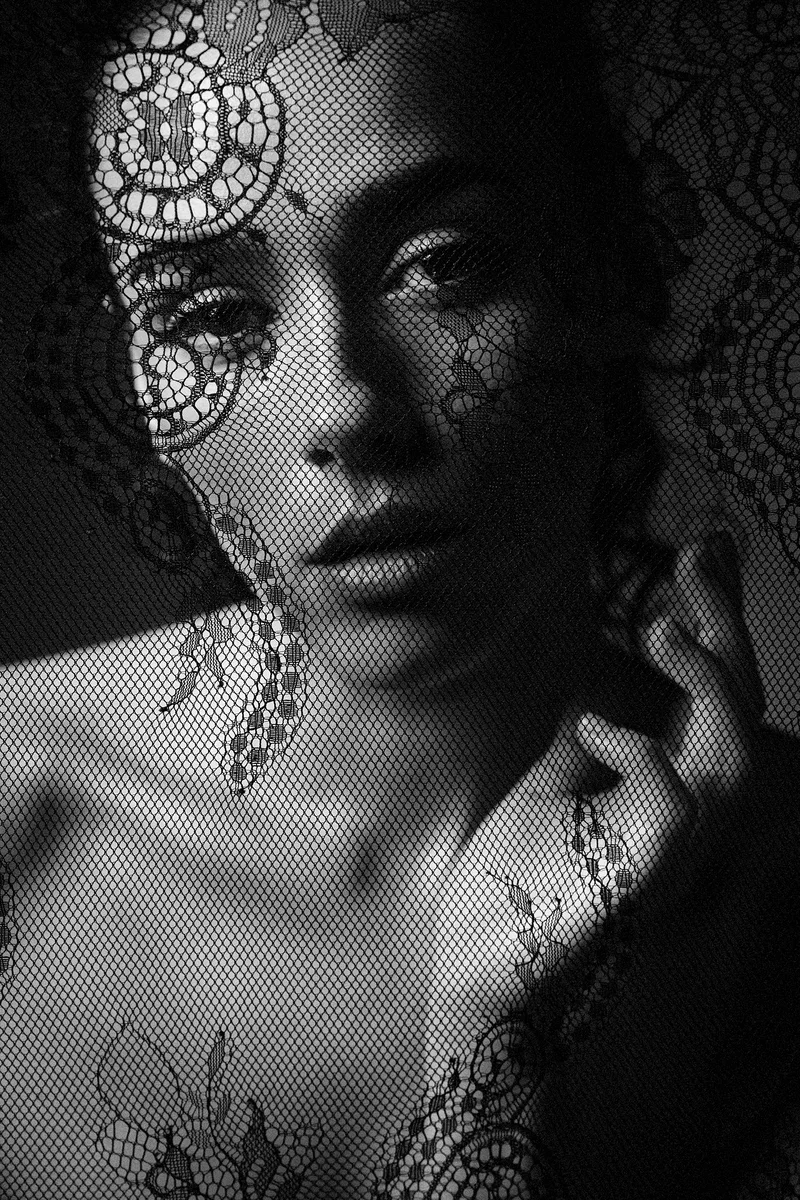 Black and white portrait of a woman with lace shadows, her hand near her face