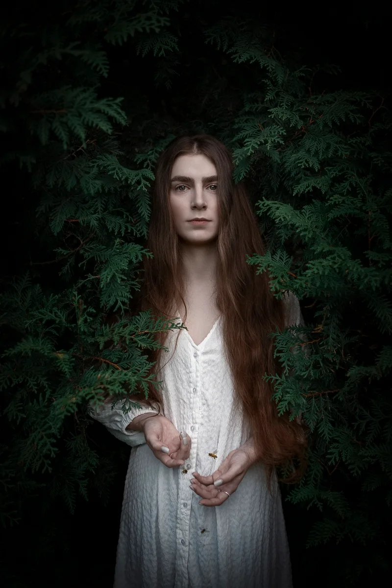 Woman in a white dress standing amid dense greenery with her hands held in front