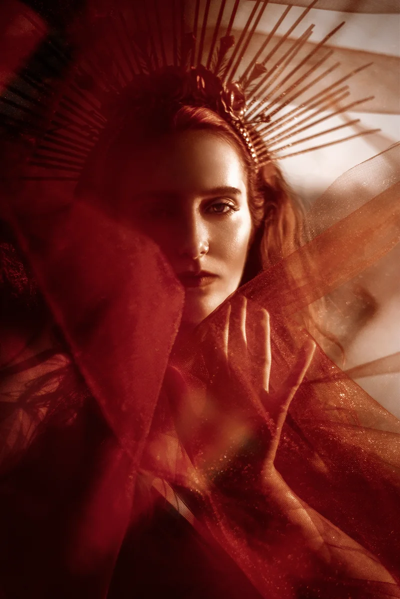 Woman's face amid red shadows and fan-shaped rays of light