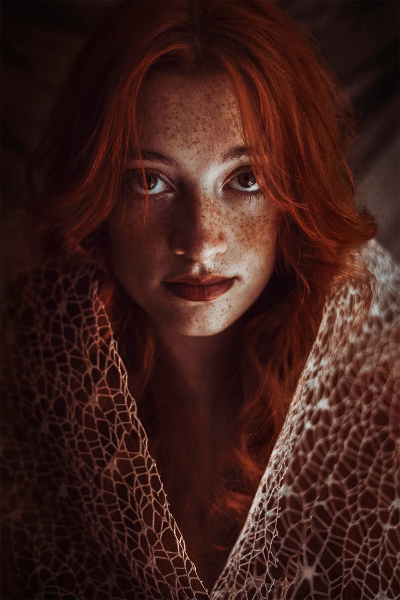 Freckled red-haired woman wrapped in a shawl with a web-like pattern
